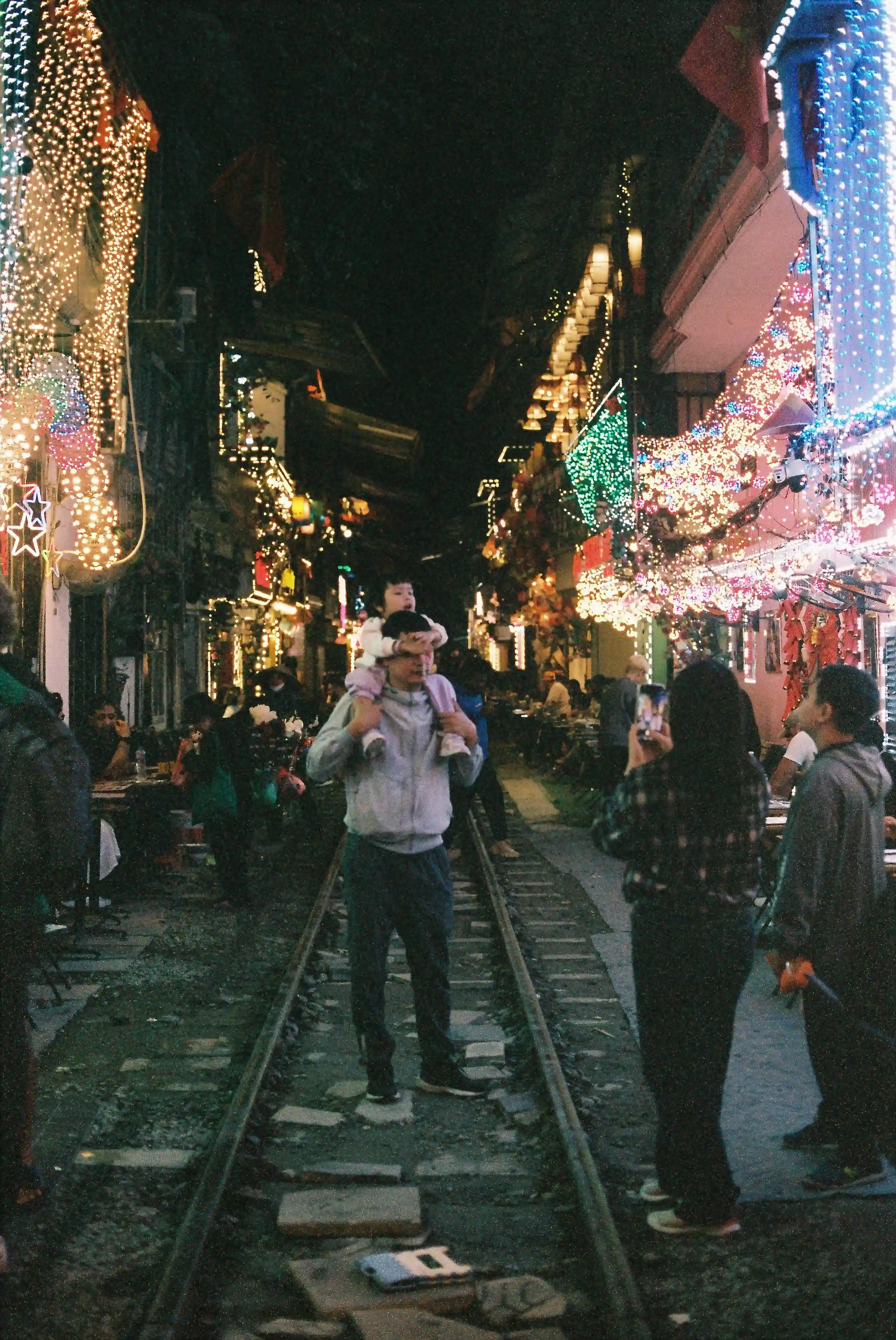 Ha Noi night train street father carrying daughter on shoulders mom taking picture