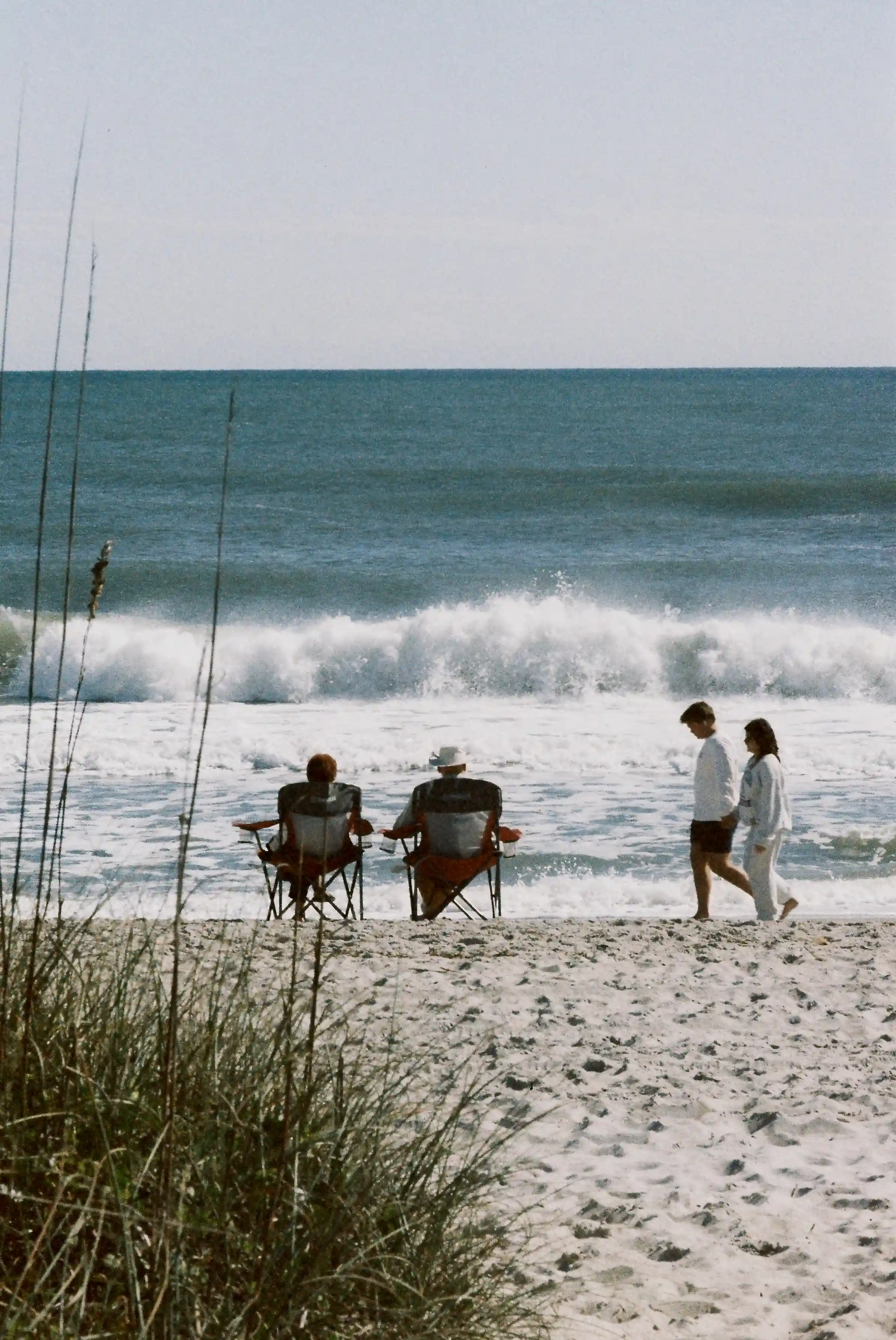 Beach situation old Couple is sitting chairs enjoying waves of ocean and young couple is crossing them
